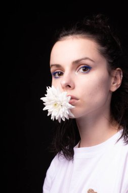 Ağzında beyaz kasımpatı tutan bir kadın, siyah arka plan.