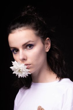 Ağzında beyaz kasımpatı tutan bir kadın, siyah arka plan.