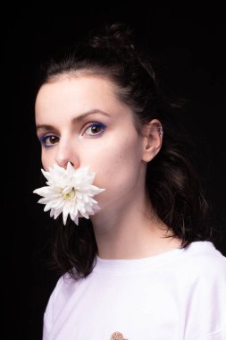 Ağzında beyaz kasımpatı tutan bir kız, siyah arka plan.