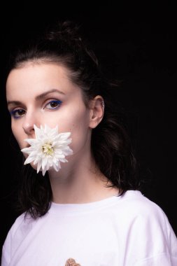 Ağzında beyaz kasımpatı tutan bir kız, siyah arka plan.