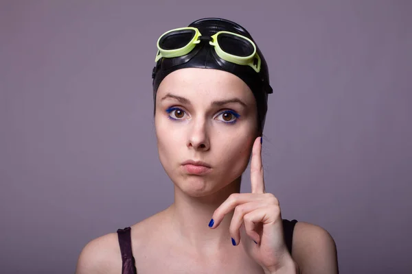 woman swimmer, in a swimming cap, glasses and a swimsuit, gray background