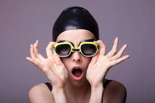 surprised woman swimmer, in a swimming cap, glasses and a swimsuit, gray background