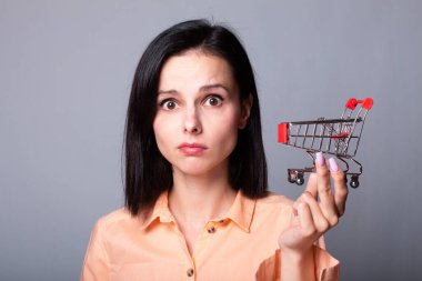 Turuncu gömlekli kadın elinde küçük bir alışveriş arabası tutuyor.