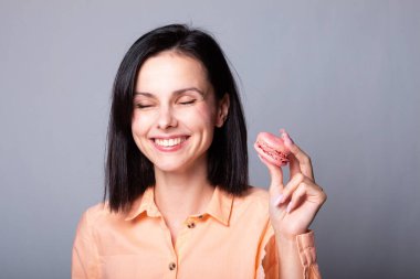 Turuncu tişörtlü gülümseyen kadın elinde Fransız kurabiyeleri, gri arka plan.