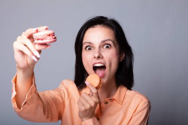 Turuncu tişörtlü gülümseyen kadın elinde Fransız kurabiyeleri, gri arka plan.