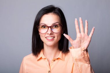 Gözlüklü, turuncu gömlekli, gri arka planlı hoş bir kadın.