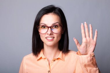 Gözlüklü, turuncu gömlekli, gri arka planlı hoş bir kadın.