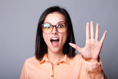 Gözlüklü, turuncu gömlekli, gri arka planlı hoş bir kadın.