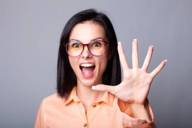 Gözlüklü, turuncu gömlekli, gri arka planlı hoş bir kadın.