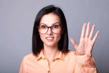 Gözlüklü, turuncu gömlekli, gri arka planlı hoş bir kadın.