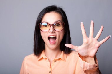 Gözlüklü, turuncu gömlekli, gri arka planlı hoş bir kadın.