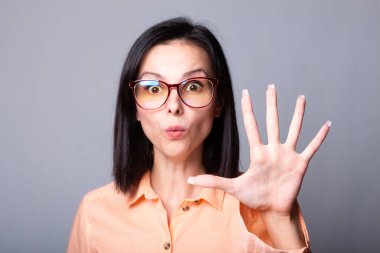 Gözlüklü, turuncu gömlekli, gri arka planlı hoş bir kadın.