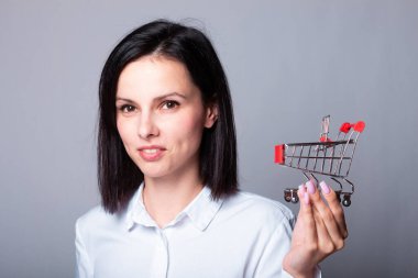 Beyaz gömlekli gülümseyen kadın elinde küçük bir alışveriş arabası, finans sembolü.