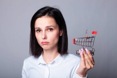 Beyaz gömlekli kadın elinde küçük bir alışveriş arabası tutuyor.