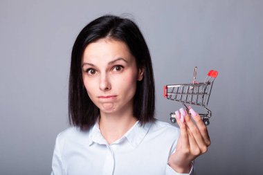 Beyaz gömlekli kadın elinde küçük bir alışveriş arabası tutuyor.