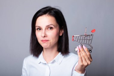 Beyaz gömlekli gülümseyen kadın elinde küçük bir alışveriş arabası, finans sembolü.