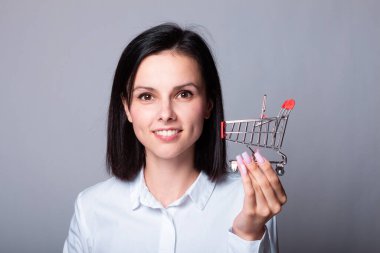 Beyaz gömlekli gülümseyen kadın elinde küçük bir alışveriş arabası, finans sembolü.