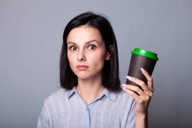 Güzel bayan ellerinde bir fincan kahve tutuyor, gri arka planda.