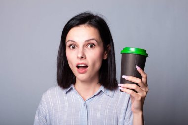 Güzel bayan ellerinde bir fincan kahve tutuyor, gri arka planda.