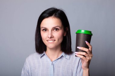 Güzel bayan ellerinde bir fincan kahve tutuyor, gri arka planda.