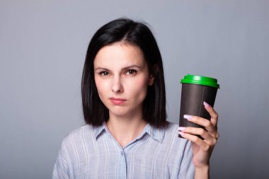 Güzel bayan ellerinde bir fincan kahve tutuyor, gri arka planda.