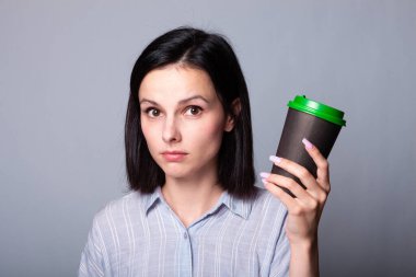 Güzel bayan ellerinde bir fincan kahve tutuyor, gri arka planda.