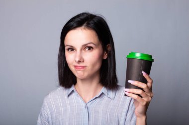 Güzel bayan ellerinde bir fincan kahve tutuyor, gri arka planda.