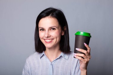 Güzel bayan ellerinde bir fincan kahve tutuyor, gri arka planda.