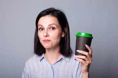 Güzel bayan ellerinde bir fincan kahve tutuyor, gri arka planda.