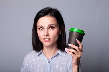 Güzel bayan ellerinde bir fincan kahve tutuyor, gri arka planda.