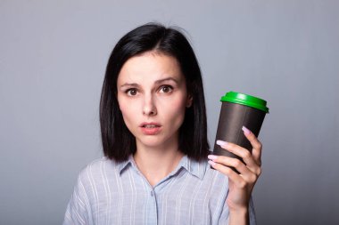 Güzel bayan ellerinde bir fincan kahve tutuyor, gri arka planda.