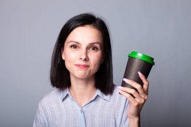 Güzel bayan ellerinde bir fincan kahve tutuyor, gri arka planda.