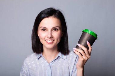 Güzel bayan ellerinde bir fincan kahve tutuyor, gri arka planda.