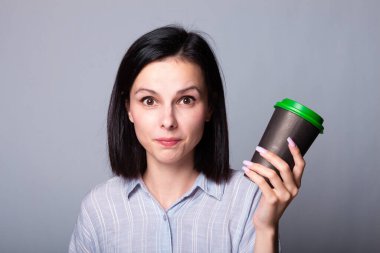 Güzel bayan ellerinde bir fincan kahve tutuyor, gri arka planda.