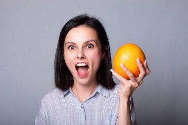 Ellerinde greyfurt tutan gömlekli bir kadın.