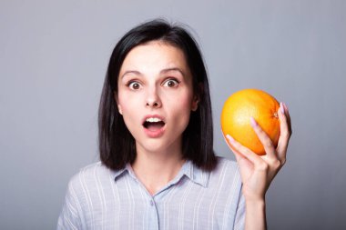 Ellerinde greyfurt tutan gömlekli bir kadın.