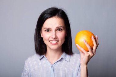 Ellerinde greyfurt tutan gömlekli bir kadın.