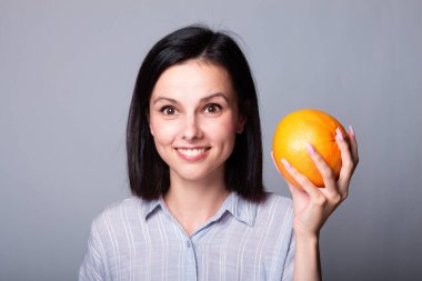 Ellerinde greyfurt tutan gömlekli bir kadın.