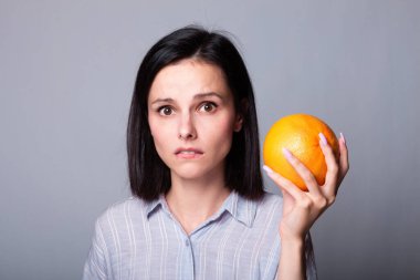 Ellerinde greyfurt tutan gömlekli bir kadın.