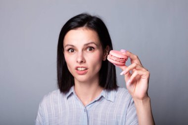 Tişörtlü gülümseyen kadın elinde Fransız kurabiyeleri, gri arka plan.