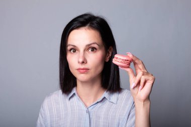 Gri tişörtlü tatlı kız ellerinde kurabiyeler, gri arka plan.