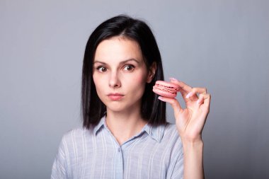 Gömlekli kadın elinde kurabiyeler, gri arka planda.