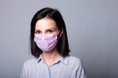 Gömlekli bir kız ve yüzünde pembe bir tıbbi maske.
