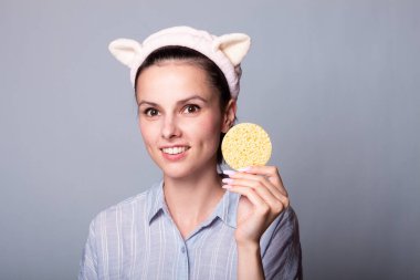 Gri arka planda süngerleri tutarken güzel, gülümseyen genç bir kadın eğleniyor.