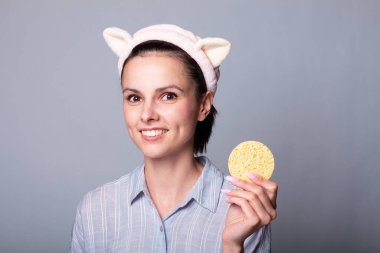 Gri arka planda süngerleri tutarken güzel, gülümseyen genç bir kadın eğleniyor.