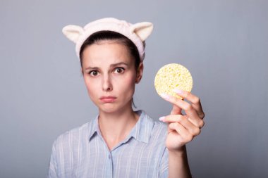 Gri arka planda kozmetik sünger tutan ve gülümseyen güzel bir kadın görüntüsü.