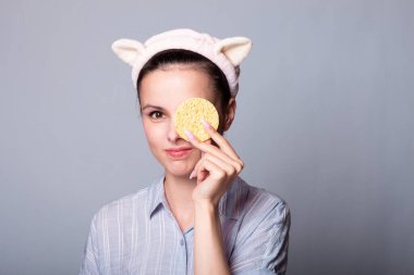 Gri arka planda kozmetik sünger tutan ve gülümseyen güzel bir kadın görüntüsü.