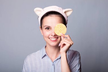 Gri arka planda süngerleri tutarken güzel, gülümseyen genç bir kadın eğleniyor.