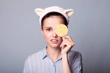 Gri arka planda kozmetik sünger tutan ve gülümseyen güzel bir kadın görüntüsü.