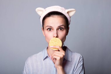 Gri arka planda süngerleri tutarken güzel, gülümseyen genç bir kadın eğleniyor.